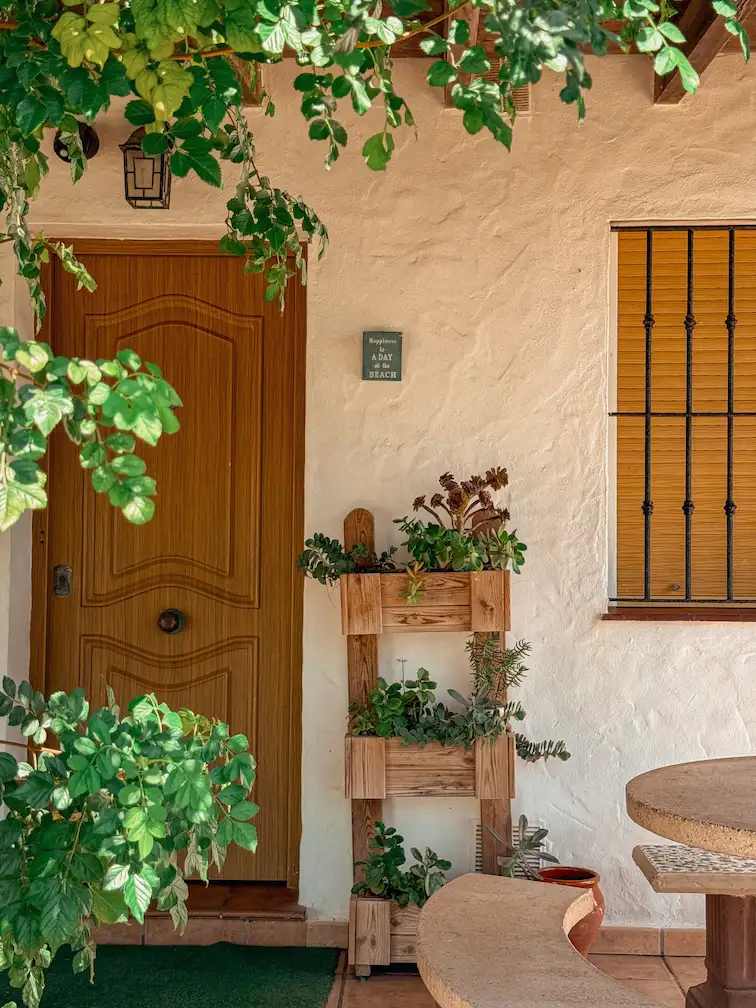 Entrada principal de la casa rural con fachada blanca y rodeada de plantas y flores.